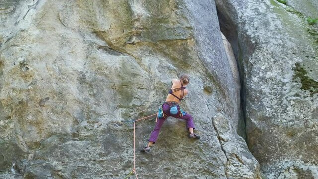 Strong female climber climbing steep wall of rocky mountain. Sportswoman overcoming difficult route. Engaging in extreme sports hobby concept