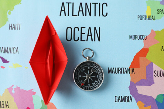 Red Paper Boat And Compass On World Map, Flat Lay