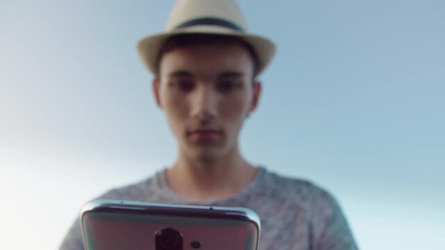 Blurred silhouette of a guy in a hat against a blue sky with a mobile phone in his hands