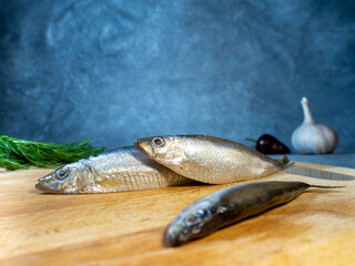 Lightly salted sprat on a cutting board. Whole fish, pepper, dill and garlic on the table.