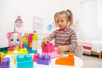 Obraz na płótnie Canvas Cute little girl playing with colorful building blocks at table in room