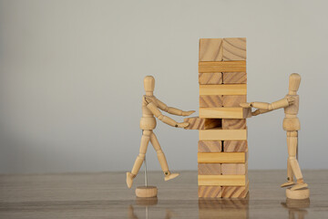 2 dolls building a wooden block tower on a table, white background. Construction business risk...