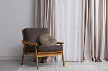 Comfortable armchair with cushion near window in living room. Interior design