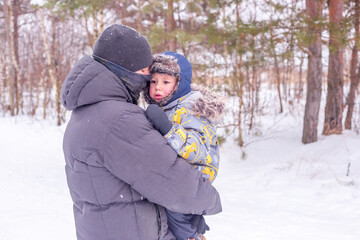 Fototapeta na wymiar Dad holds and hugs his little son in a snowy forest or winter park.