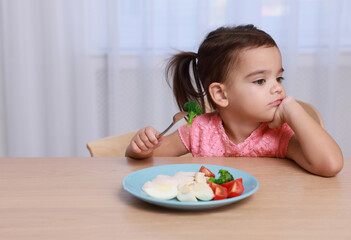 Cute little girl refusing to eat her breakfast at home, space for text