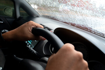 Abstract Hand of driving man use car steering wheel in side of car. Driving a leafy car on a rainy...