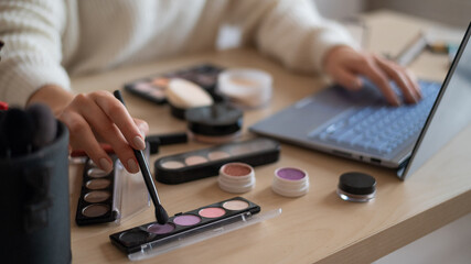 A faceless woman watches online training from a professional makeup artist on a laptop. Distance...