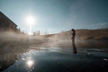 Woman relaxing at hot spring. First frost, hot water, beautiful wooden house in colourful autumn landscape