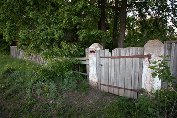 old wooden gate with concrete pillars leading to a grove of trees