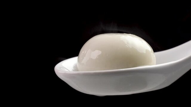 Fresh and hot Tangyuan rice dumpling ball in a white spoon over black background.