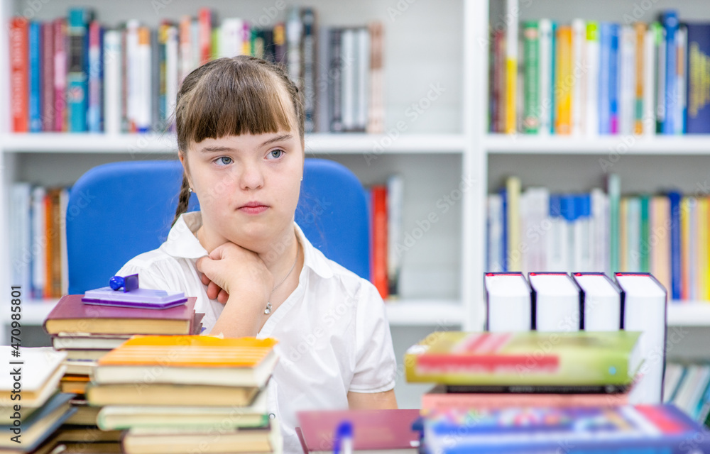 Wall mural smart girl with syndrom down needs sits with books at library