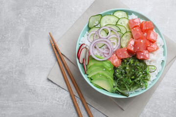 Delicious poke bowl with salmon, seaweed and vegetables served on light grey table, flat lay