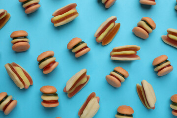 Tasty jelly candies in shape of burger and hot dog on light blue background, flat lay