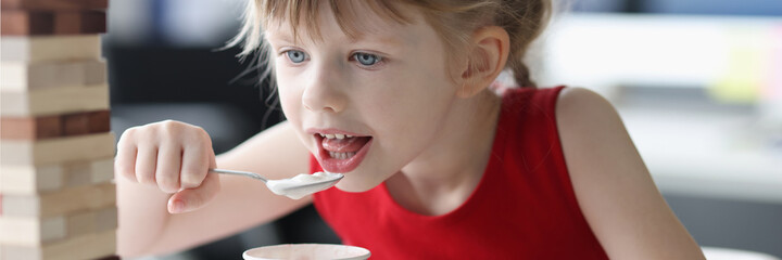 Little girl eating ice cream with spoon from plastic cup at home