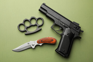 Black brass knuckles, gun and knife on green background, flat lay
