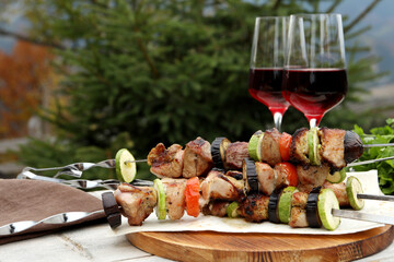 Metal skewers with delicious meat, vegetables and wine served on wooden table outdoors