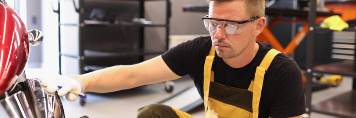 Man repairman in goggles picking up paint to motorcycle in car repair shop