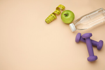 Dumbbells, bottle of water, apple, measuring tape on beige background