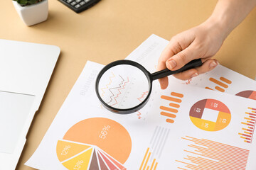 Woman with magnifier and business charts on beige background, closeup