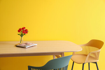 Flowers and magazine on wooden table near color wall