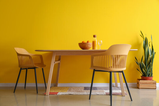 Interior of dining room with wooden table, chairs and houseplant near yellow wall
