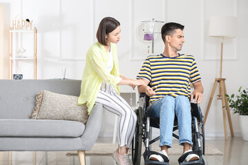 Fototapeta na wymiar Young woman and her husband in wheelchair undergoing medical rehabilitation at home