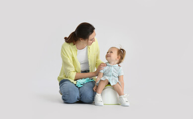 Mother potty training her little daughter on light background