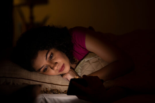 Woman Watching Smartphone Alone At Night While Lying On Bed 