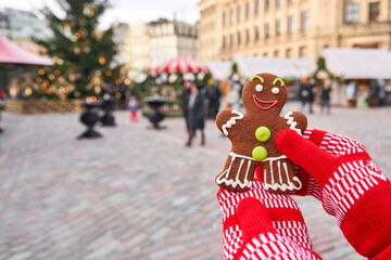 Coffee cup and a smiling gingerbread man in hands. Christmas mood in blurred background. Christmas market in old town European small city.