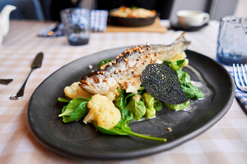 Roasted pike perch or cod fish with baked vegetables and spinach. Dish decorated with a slice of lemon. Restaurant menu