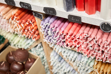 Many multicolored colorful paraffin stick Pastel colors candles arranged in shelves lying on shelter and sorted by color in a household candle shop store market.