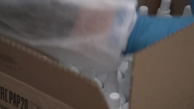 Close up of manual packing white antiseptic bottles to corrugated cardboard box on table by gloved hands. Bottles with labels but can't see