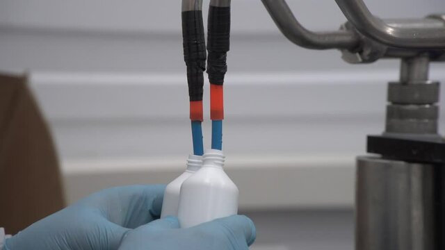 Close up of manual filling two bottles by small tubes and gloved hands with out of focus wall on background