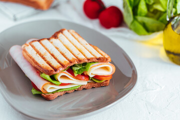 Toast sandwich with gouda cheese and turkey ham filled with tomato and lettuce on a bright background with ingredients in blurry background