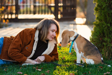 Woman walking with beagle puppy in backyard. Owner lies on green grass and teaches pet commands...