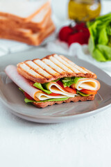 Toast sandwich with gouda cheese and turkey ham filled with tomato and lettuce on a bright background with ingredients in blurry background