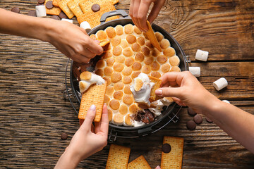 Women eating tasty S'mores dip at wooden table