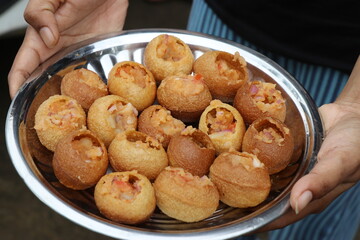 Hand holding a plate of homemade gol gappa or a few call as Pani puri balls stuffed with potato and...