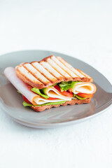 Toast sandwich with gouda cheese and turkey ham filled with tomato and lettuce on a bright background with ingredients in blurry background
