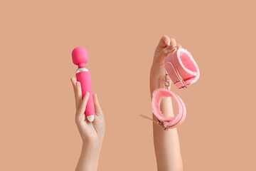 Female hands with vibrator and handcuffs on color background