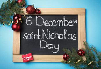 Small chalkboard with text 6 December Saint Nicholas Day and festive decor on light blue background, flat lay