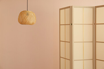 Stylish folding screen and wicker lamp on wall background