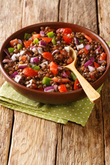 Green lentil salad with tomatoes, onions and chili peppers close-up in a plate on the table. vertical