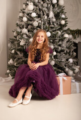 a girl in a dress sits at a festive party at the Christmas tree in a beautiful dress