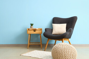 Stylish interior with wooden bedside table and armchair near blue wall