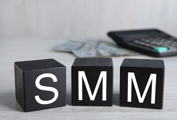 Black cubes with abbreviation SMM (Social media marketing), money and calculator on white wooden...