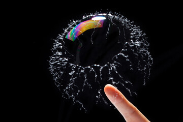 transparent soap bubble burst by a finger on black background.