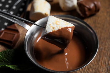 Dipping tasty grilled marshmallow in chocolate on wooden background