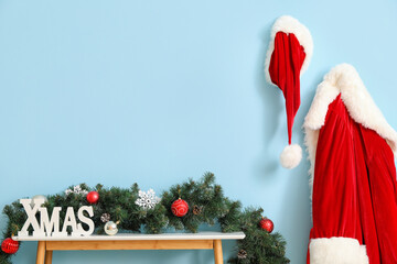 Decorated table with word XMAS and Santa Claus costume hanging on color wall