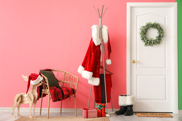Hanger with Santa Claus costume, boots and chair with plaid near color wall